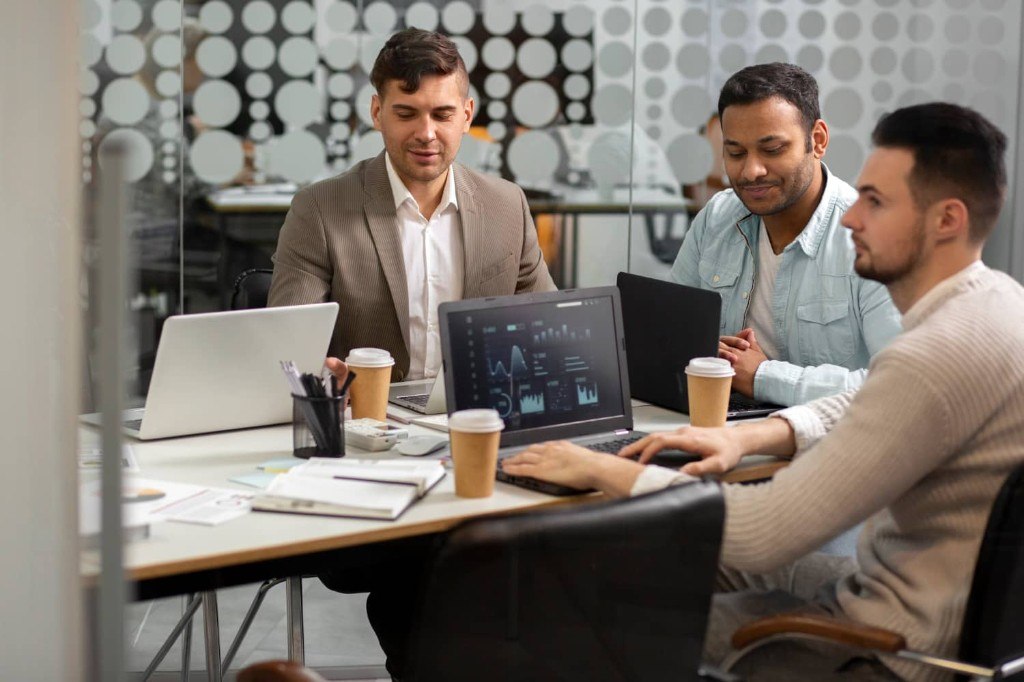Team collaborating around laptops while applying AI tools to real business work